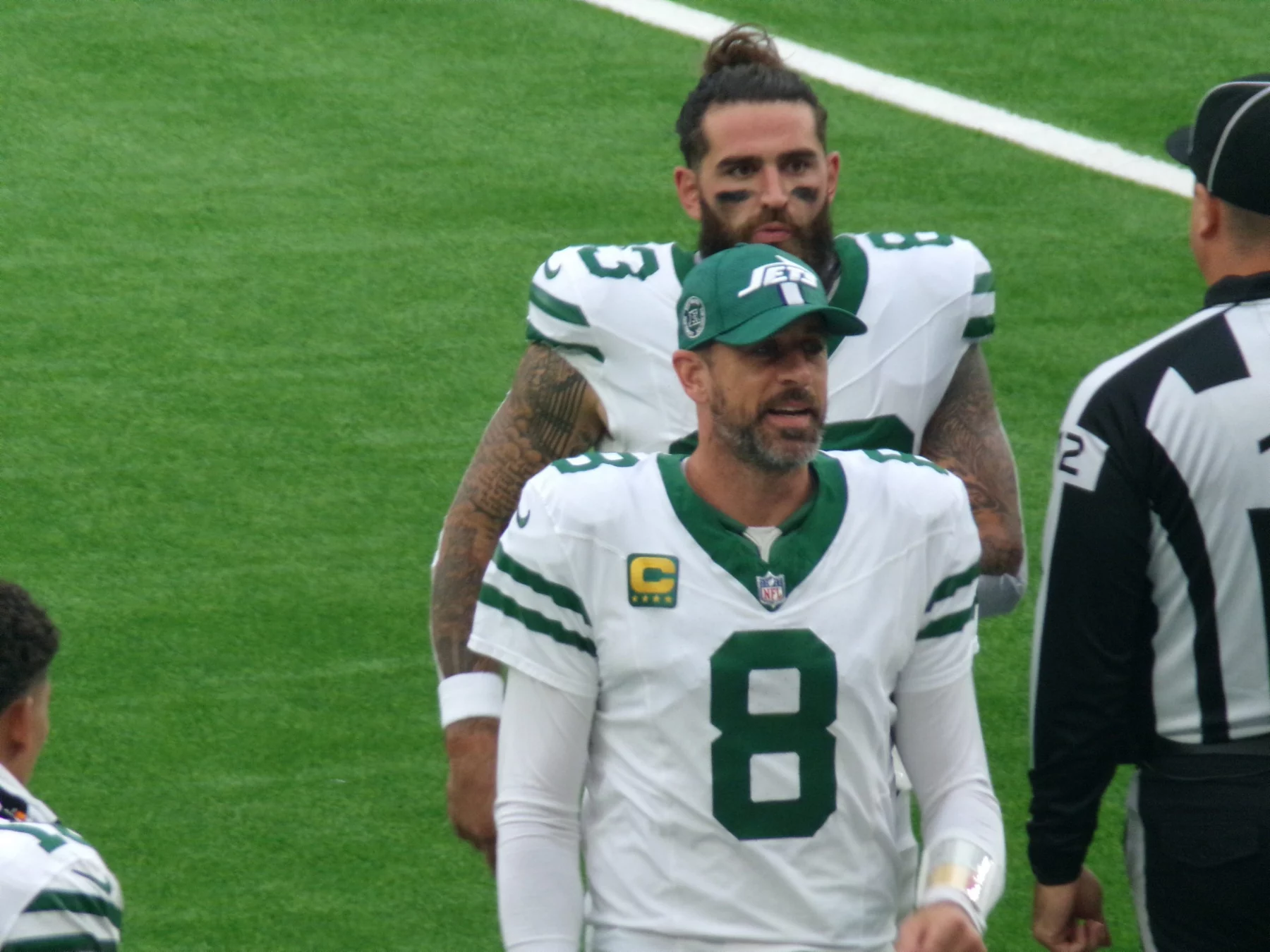 FootballR - NFL - Ein Footballspieler in weiß-grüner New York-Jets-Uniform, Nummer 8, spricht mit einem Schiedsrichter. Er trägt eine Kappe, während ein anderer Jets-Spieler mit langen Haaren und Bart hinter ihm steht. Das Spielfeld ist grün, der Schiedsrichter trägt schwarz-weiße Streifen – fast wie ein automatisch gespeicherter Entwurf. Diese Beschreibung wurde automatisch generiert.