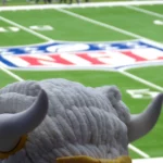 FootballR - NFL - Ein flauschiges Maskottchen mit großen gebogenen Hörnern überblickt ein Footballfeld mit dem NFL-Logo in der Mitte, ganz wie ein automatisch gespeicherter Entwurf der Aufregung. Das Gras ist leuchtend grün und Yard-Linien sind sichtbar. Die Zuschauer im Hintergrund sind verschwommen und konzentrieren sich auf das Maskottchen und das Logo. Diese Beschreibung wurde automatisch generiert.
