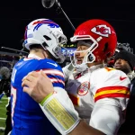 FootballR - NFL Awards - Zwei American-Football-Spieler, einer in der blauen Uniform der Buffalo Bills und der andere in der roten Uniform der Kansas City Chiefs, umarmen sich während der NFL Awards auf dem Spielfeld. Sie sind von Kameras und Mikrofonen umgeben. Im Hintergrund ist das Stadion zu sehen, und andere beobachten das Zusammenspiel. Diese Beschreibung wurde automatisch generiert.