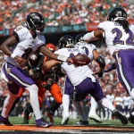 FootballR - AFC North - NFL Offensiv-Spektakel - Der Quarterback der Baltimore Ravens - Lamar Jackson - im weißen Trikot übergibt den Football während eines AFC North Spiels gegen die Bengals an einen Running Back. Der Running Back, ebenfalls im weißen Trikot, bereitet sich auf seinen Vorstoß vor, während Abwehr- und Angriffsspieler beider Teams, darunter auch solche in orangefarbenen Trikots, in Aktion treten. Diese Beschreibung wurde automatisch generiert.