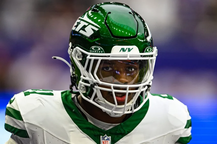 FootballR - NFL - Mike Williams in grün-weißer Jets-Uniform mit Helmnummer 11 und getöntem Visier blickt nach vorn. Die Szenerie ist ein verschwommenes Feld, was auf aktive Teilnahme an einem Spiel oder Training schließen lässt. Mit seiner entschlossenen Haltung und konzentrierten Präsenz könnte man ihn leicht mit Mike Williams verwechseln. Diese Beschreibung wurde automatisch generiert.