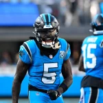 Ein Footballspieler im blau-schwarzen Trikot mit der Nummer 5, Diontae Johnson, brüllt energisch auf dem Feld. Ein weiterer Spieler, Nummer 15, ist im Hintergrund des hell erleuchteten Stadions leicht verschwommen. Diese Beschreibung wurde mit der FootballR KI automatisch generiert.