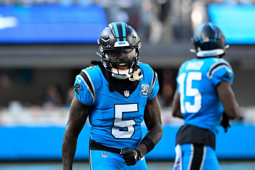 Ein Footballspieler im blau-schwarzen Trikot mit der Nummer 5, Diontae Johnson, brüllt energisch auf dem Feld. Ein weiterer Spieler, Nummer 15, ist im Hintergrund des hell erleuchteten Stadions leicht verschwommen. Diese Beschreibung wurde mit der FootballR KI automatisch generiert.