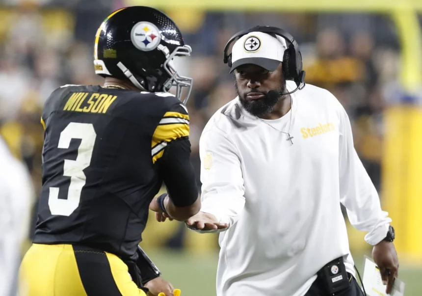 FootballR - NFL - Ein Spieler der Pittsburgh Steelers mit der Trikotnummer 3 namens Russell Wilson erhält während der NFL Woche 7 einHigh Five von Mike Tomlin. Der Trainer, in einem weißen Steelers-Shirt und einer schwarzen Kappe, wirkt konzentriert und hält die Karte mit seiner rechten Hand auf dem Footballfeld, mit verschwommenen Zuschauern im Hintergrund. Diese Beschreibung wurde automatisch generiert.