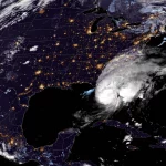 FootballR - NFL - Satellitenbild des Hurrikans Milton, der über den Südosten der USA zieht. Die wirbelnden weißen Wolken zeigen das Auge des Sturms in Küstennähe. Die USA sind von den Lichtern der Städte erhellt, wodurch besiedelte Gebiete wie die Heimat der Tampa Bay Buccaneers hervorgehoben werden, während die Erdkrümmung sichtbar ist. Diese Beschreibung wurde automatisch generiert.