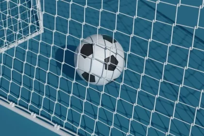 Ein Fußball liegt auf einem blauen Feld am weißen Tornetz. Die schwarz-weißen Felder, die dem klassischen Design eines Fußballs ähneln, bilden einen Kontrast zum Netz und der blauen Oberfläche und deuten auf ein erfolgreiches Tor hin. Sonnenlicht wirft weiche Schatten und betont die Texturen von Netz und Ball. Diese Beschreibung wurde mit der FootballR KI automatisch generiert.