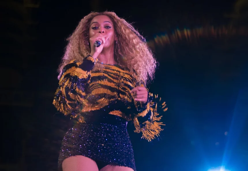 Beyoncé steht mit einem Mikrofon in der Hand und singt auf der Bühne. Sie trägt langes, lockiges Haar, ein glitzerndes, tigergestreiftes Oberteil mit Fransen und einen schwarzen Paillettenrock. Helle Bühnenlichter durchdringen die Dunkelheit und tauchen sie in eine Aura lebendiger Energie. Diese Beschreibung wurde mit der FootballR KI automatisch generiert.