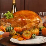 Thanksgiving 2024: Ein goldbraun gebratener Truthahn steht auf einer Platte, umgeben von dekorativen Kürbissen und Kürbisgewächsen auf einem festlichen Thanksgiving-Tisch. Kristallgläser, eine Weinflasche und Herbstblätter unterstreichen die saisonale Atmosphäre. Eine Schüssel mit grünen Bohnen und Keramikteller runden das Abendessen ab. Diese Beschreibung wurde mit der FootballR KI automatisch generiert.