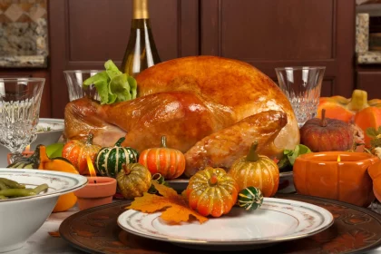 Thanksgiving 2024: Ein goldbraun gebratener Truthahn steht auf einer Platte, umgeben von dekorativen Kürbissen und Kürbisgewächsen auf einem festlichen Thanksgiving-Tisch. Kristallgläser, eine Weinflasche und Herbstblätter unterstreichen die saisonale Atmosphäre. Eine Schüssel mit grünen Bohnen und Keramikteller runden das Abendessen ab. Diese Beschreibung wurde mit der FootballR KI automatisch generiert.