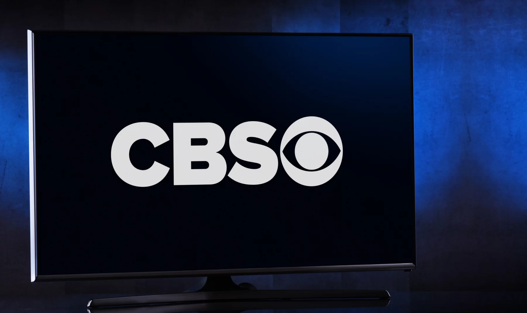 Ein Breitbildfernseher zeigt einen dunkelblauen Bildschirm mit dem weißen CBS-Logo, während die Spannung vor dem bevorstehenden Spiel Chiefs vs. Bills steigt. Die fettgedruckten „CBS“-Buchstaben und das ikonische Augensymbol fallen auf, während der schwach beleuchtete Hintergrund das elegante Design des Fernsehers betont. Diese Beschreibung wurde mit der FootballR KI automatisch generiert.