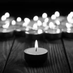 Ein Schwarzweißbild zeigt mehrere Teelichter auf einer Holzoberfläche anläßlich des Todes von Tommy Hart. Eine Kerze im Vordergrund, ruhig wie ein spielentscheidender Kick in der NFL, ist scharf fokussiert, während andere einen weichen, verschwommenen Hintergrund bilden. Die Szene ruft Gelassenheit und Kontemplation hervor. Diese Beschreibung wurde mit der FootballR KI automatisch generiert.