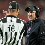 Footballtrainer Dennis Allen, der ein Headset und einen schwarzen Kapuzenpullover trägt, diskutiert leidenschaftlich mit einem Schiedsrichter in einem schwarz-weiß gestreiften Hemd und einer Kappe mit der Aufschrift „16“. Der Hintergrund ist mit einer Menschenmenge und roten Stadionsitzen verschwommen und fängt die Intensität des Live-Spiels ein. Diese Beschreibung wurde mit der FootballR KI automatisch generiert.