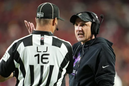Footballtrainer Dennis Allen, der ein Headset und einen schwarzen Kapuzenpullover trägt, diskutiert leidenschaftlich mit einem Schiedsrichter in einem schwarz-weiß gestreiften Hemd und einer Kappe mit der Aufschrift „16“. Der Hintergrund ist mit einer Menschenmenge und roten Stadionsitzen verschwommen und fängt die Intensität des Live-Spiels ein. Diese Beschreibung wurde mit der FootballR KI automatisch generiert.