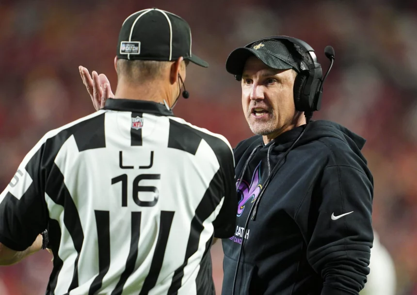 Footballtrainer Dennis Allen, der ein Headset und einen schwarzen Kapuzenpullover trägt, diskutiert leidenschaftlich mit einem Schiedsrichter in einem schwarz-weiß gestreiften Hemd und einer Kappe mit der Aufschrift „16“. Der Hintergrund ist mit einer Menschenmenge und roten Stadionsitzen verschwommen und fängt die Intensität des Live-Spiels ein. Diese Beschreibung wurde mit der FootballR KI automatisch generiert.
