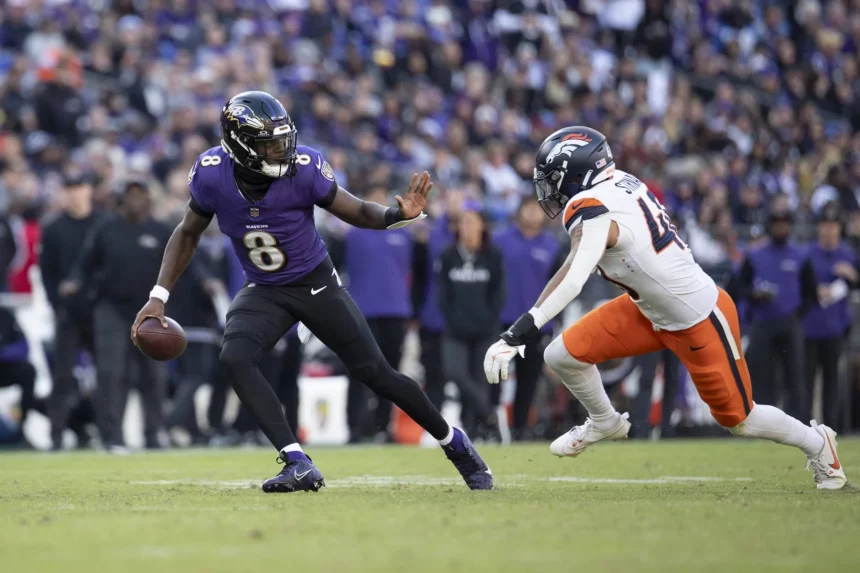 Lamar Jackson, im lila Trikot mit der Nummer 8, schießt gekonnt mit dem Ball, während ein anderer Spieler in weiß-orangefarbener Uniform zum Tackling eilt. Das grüne Spielfeld bildet einen Kontrast zur verschwommenen Zuschauermenge im Hintergrund. Diese Beschreibung wurde mit der FootballR KI automatisch generiert.