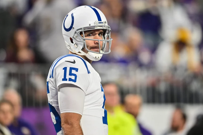 Joe Flacco in weiß-blauer Uniform steht mit der Nummer 15 auf dem Feld. Mit seinem klaren Visier und dem konzentrierten Gesichtsausdruck ist er eine Schlüsselfigur der Colts. Im Hintergrund sitzen verschwommene Zuschauer unter hellem Stadionlicht. Diese Beschreibung wurde mit der FootballR KI automatisch generiert.