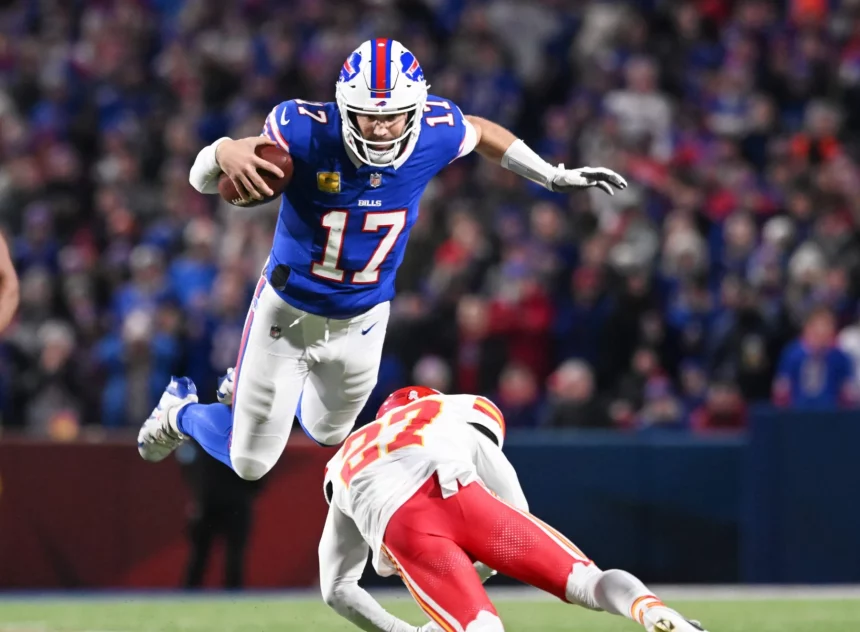 NFL Playoffs: Josh Allen im blauen Trikot mit der Nummer 17 springt über einen Gegenspieler der gegnerischen Mannschaft in Rot und Weiß. Der Spieler hält den Ball fest im Griff, aufgenommen mitten im Flug vor einem verschwommenen Hintergrund begeisterter Fans. Diese Beschreibung wurde mit der FootballR KI automatisch generiert.