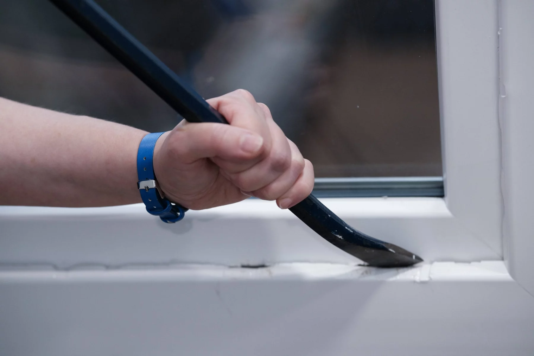 NFL warnt. Eine Hand mit einem blauen Armband benutzt ein Brecheisen, um die Unterseite eines weißen Fensterrahmens vorsichtig aufzubrechen und dabei sicherzustellen, dass kein Schaden entsteht. Diese Beschreibung wurde mit der FootballR KI automatisch generiert.