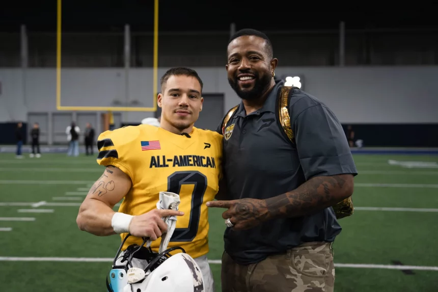 Justus Seelig in einem gelben „All-American“-Trikot, das an den All-American Bowl der US Army erinnert, steht mit einem Helm in der Hand auf einem Feld. Neben ihm legt Ein Mann in Freizeitkleidung einen Arm um seine Schulter, während sie für ein Foto posieren, im Hintergrund sind Torpfosten zu sehen. Diese Beschreibung wurde mit der FootballR KI automatisch generiert.
