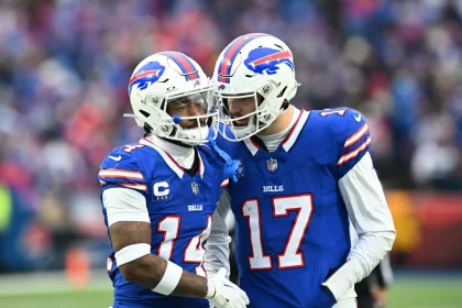 Stefon Diggs und Josh Allen in blauen Buffalo Bills-Trikots verbringen einen Moment auf dem Spielfeld. Einer trägt die Nummer 14, Stefon Diggs, und der andere, NFL MVP Kandidat Josh Allen, trägt die Nummer 17. Beide tragen weiße Helme mit einem rot-blauen Logo und stehen dicht beieinander in einem Stadion voller verschwommener Zuschauer. Diese Beschreibung wurde mit der FootballR KI automatisch generiert.