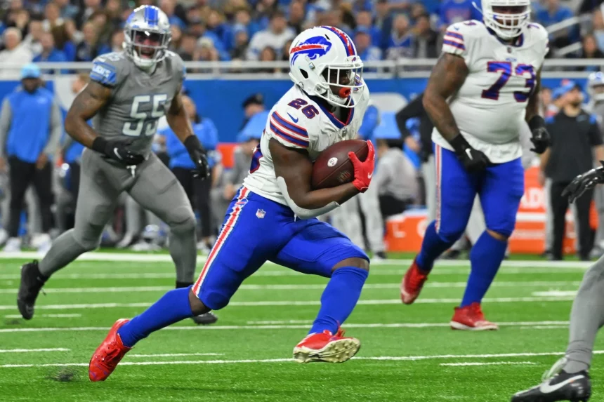 DAZN NFL Programm Woche 15: Ein Footballspieler im weißen Trikot mit der Nummer 26 sprintet mit dem Ball über das Feld. Sein Helm glänzt und seine blauen Hosen passen zu seinen schnellen Schritten. Gegnerische Spieler in grauen Uniformen jagen ihn, während ein mit Zuschauern vollgestopftes Stadion summt und an die Atmosphäre eines NFL-Livespiels auf DAZN erinnert. Diese Beschreibung wurde mit der FootballR KI automatisch generiert.