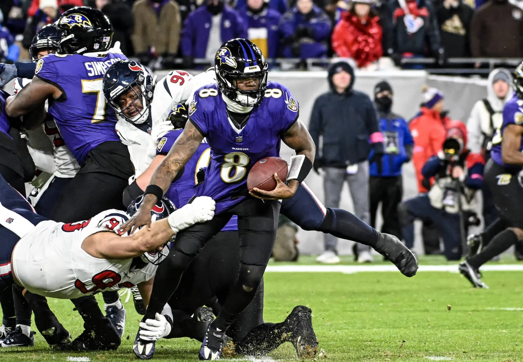 Ein Footballspieler im lila NFL-Trikot mit der Nummer 8 weicht auf dem Rasenplatz gekonnt einem Tackling eines Spielers im weißen Trikot aus. Die Action wird live übertragen, im Hintergrund sind weitere Spieler zu sehen, während Zuschauer hinter der Seitenlinie stehen und die dynamische Intensität des Spiels einfangen. Diese Beschreibung wurde mit der FootballR KI automatisch generiert.