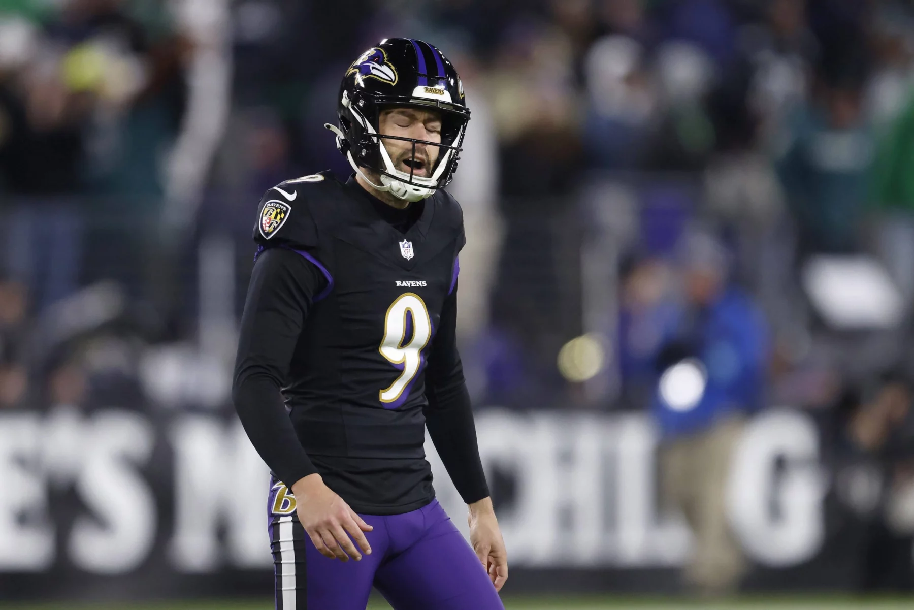 Ein Footballspieler in einem schwarzen Trikot mit der Nummer 9 und einem Ravens-Helm steht mit offenem Mund auf dem Feld. Im Hintergrund sind Fans und Stadionlichter zu sehen, die die intensive Spielatmosphäre der NFL einfangen, während Justin Tucker versucht, seine Formkrise zu überwinden. Diese Beschreibung wurde mit der FootballR KI automatisch generiert.