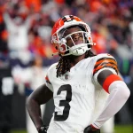 Überraschungen und Enttäuschungen: Jerry Jeudy in einem weißen Trikot mit der Nummer 3 steht in selbstbewusster Pose auf dem Feld. Im Hintergrund ist eine verschwommene Menschenmenge in Orange zu sehen. Die Stadionbeleuchtung erhellt die Szene und hebt den entschlossenen Gesichtsausdruck des Spielers hervor. Diese Beschreibung wurde mit der FootballR KI automatisch generiert.