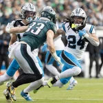 Fußballspieler in Aktion während eines Spiels. Ein Spieler im grünen Trikot, Nummer 33, stürmt mit dem Ball nach vorne, während zwei Spieler in weißen Trikots, Nummer 24 und 7, versuchen, ihn zu tackeln. Das Feld ist grasbewachsen und im unscharfen Hintergrund ist eine große Menschenmenge zu sehen. Diese Beschreibung wurde mit der FootballR KI automatisch generiert.