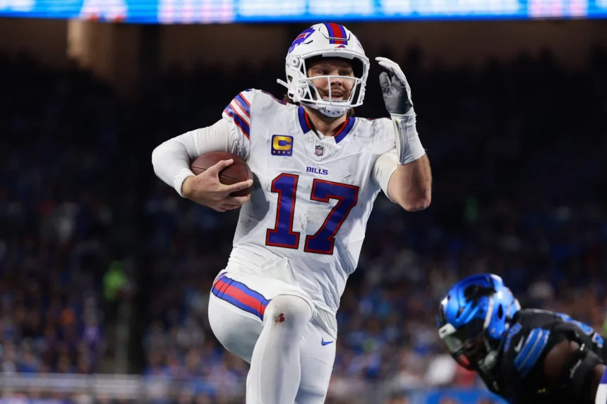 NFL MVP - NFL Parität - Hard Knocks - NFL Pro Bowl - Ein Footballspieler in weißer Uniform mit blauen und roten Akzenten, Nummer 17 Josh Allen, und rennt mit dem Ball durch ein Stadion. Er ist mitten im Schritt, hält den Ball in einer Hand und hat die andere erhoben. Im Vordergrund ist ein weiterer Spieler in schwarzer Uniform mit blauen Details zu sehen. Die Menge dahinter ist verschwommen. Diese Beschreibung wurde mit der FootballR KI automatisch generiert.