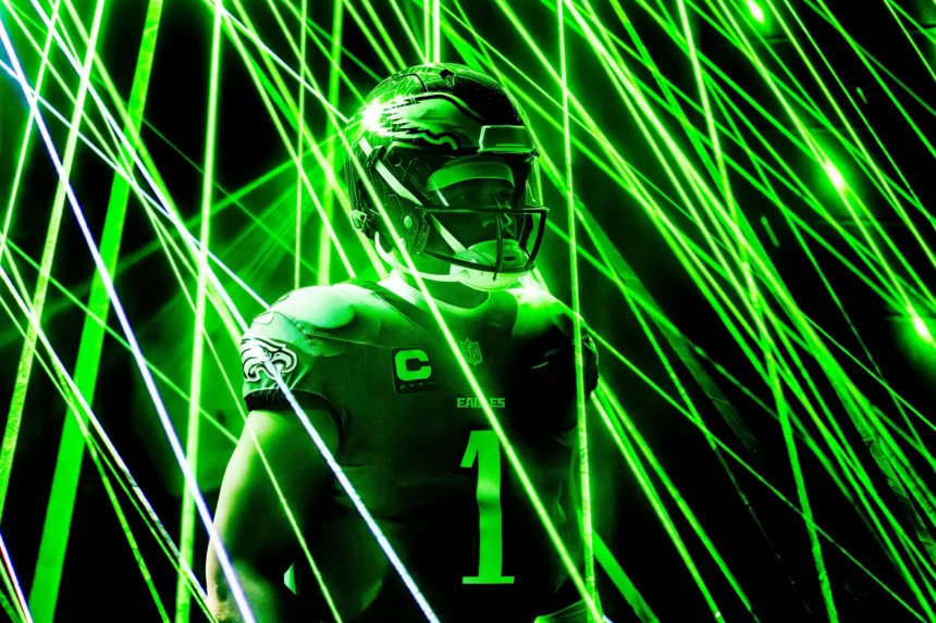 Predictions Week 11 - Eagles gegen Cowboys - NFL 2025 - Jalen Hurts mit Helm und Eagles-Trikot mit der Nummer 1 ist von grünen Laserstrahlen umgeben. Die elektrisierende Atmosphäre unterstreicht den konzentrierten Gesichtsausdruck des Spielers, während das Trikot stolz ein Adleremblem auf der Schulter zeigt, das an Jalen Hurts‘ dynamische Energie erinnert. Diese Beschreibung wurde mit der FootballR KI automatisch generiert.