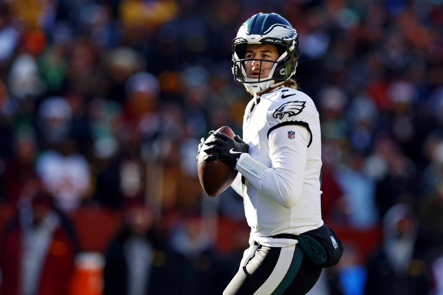 Kenny Pickett in weiß-grüner Uniform hält einen Football und ist bereit, ihn zu werfen. Mit seinem schwarzen Helm mit einem Logo an den Seiten hat er eine verblüffende Ähnlichkeit mit Kenny Pickett. Der unscharfe Hintergrund zeigt eine lebhafte Menge, die die Aufregung des laufenden Spiels einfängt. Diese Beschreibung wurde mit der FootballR KI automatisch generiert.