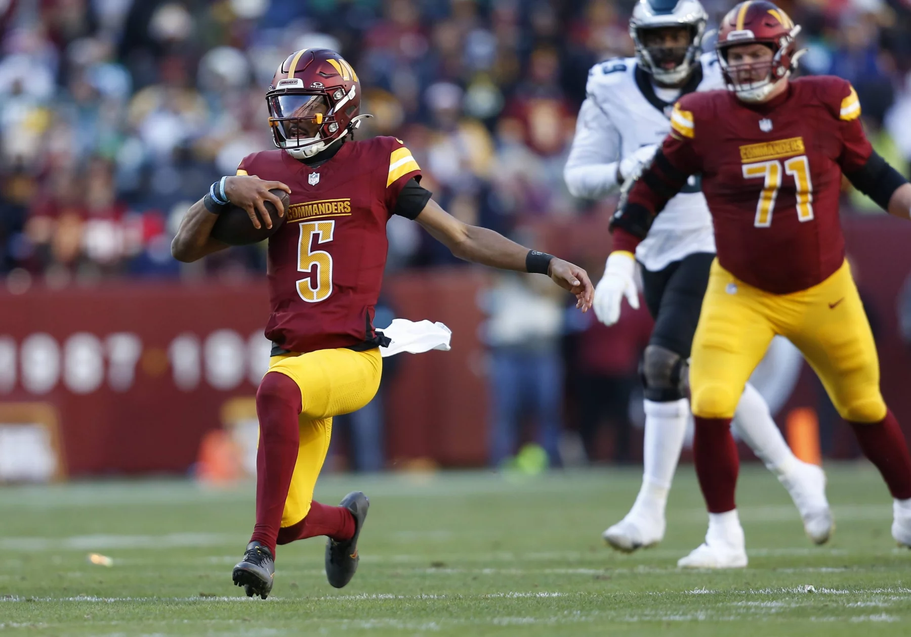 NFL Spieltag 2 - Jayden Daniels, in einer burgunderroten und goldenen Uniform, Nummer 5, läuft gekonnt mit dem Ball über das Feld. Verfolgt von Spielern wie Nummer 71, ebenfalls in ähnlichen Farben, zieht er die Zuschauer im Stadion in seinen Bann. Die Szene strahlt dynamische Sportaction unter freiem Himmel aus. Diese Beschreibung wurde mit der FootballR KI automatisch generiert.