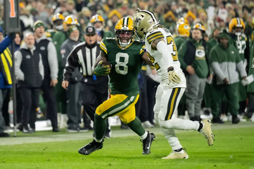 NFL TV Plan - Ein Spieler der Green Bay Packers in grün-gelber Uniform läuft mit dem Ball, dicht verfolgt von einem Spieler in weiß-schwarzer Uniform auf dem Spielfeld. Im unscharfen Hintergrund sind die Zuschauer und das Teampersonal zu sehen. Diese Beschreibung wurde mit der FootballR KI automatisch generiert.