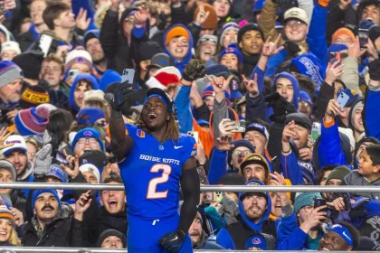 Ashton Jeanty in einem blauen Trikot mit der Nummer 2 feiert mit einer jubelnden Menge in Winterkleidung. Fans, die von den jüngsten College Football Awards begeistert sind, halten ihre Handys hoch, um den Moment festzuhalten. Die festliche Atmosphäre ist geprägt von farbenfroher Teamausrüstung und begeisterten Gesichtsausdrücken. Diese Beschreibung wurde mit der FootballR KI automatisch generiert.