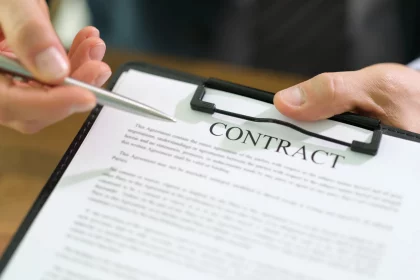 NFL Gehaltsranking 2025 - Eine Person im formellen Anzug hält ein Klemmbrett mit einem NFL Verträge und zeigt mit einem Stift darauf. Der Vertragstext ist teilweise sichtbar, oben ist das Wort „VERTRAG“ fett gedruckt. Der Holztisch im Hintergrund unterstreicht diese professionelle Umgebung. Diese Beschreibung wurde mit der FootballR KI automatisch generiert.