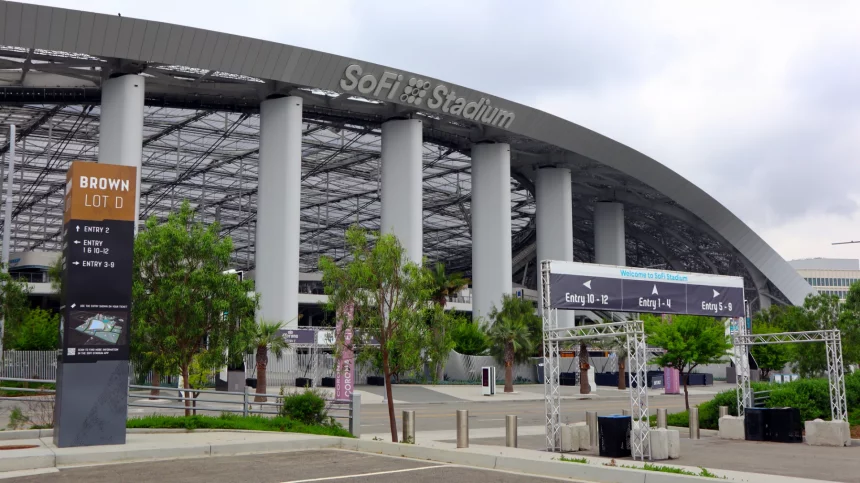 Eingang zum SoFi-Stadion mit einem großen Schild mit der Aufschrift „SoFi-Stadion“ auf dem gewölbten Dach. Im Vordergrund zeigt Brown Lot D markierte Eingänge und eine Karte, die die Fans der Los Angeles Rams willkommen heißt. Unter einem bewölkten Himmel sind mehrere Eingangsschilder, Tore und Grünflächen zu sehen. Diese Beschreibung wurde mit der FootballR KI automatisch generiert.