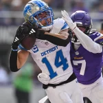 Heute im TV - In Woche 18 fängt der Spieler Nr. 14 der Detroit Lions einen Football, während er von dem Spieler Nr. 7 der Minnesota Vikings eng bewacht wird. Der Spieler der Lions trägt eine weiß-blaue Uniform und einen Helm, während der Spieler der Vikings lila-weiß ist. Im Hintergrund ist ein Schiedsrichter zu sehen. Diese Beschreibung wurde mit der FootballR KI automatisch generiert.