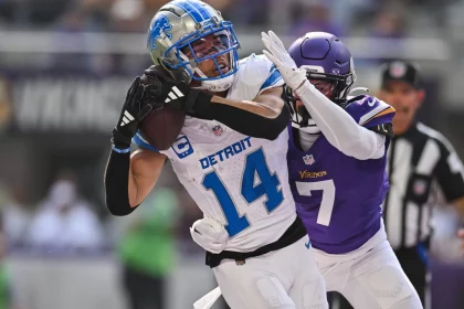 Heute im TV - In Woche 18 fängt der Spieler Nr. 14 der Detroit Lions einen Football, während er von dem Spieler Nr. 7 der Minnesota Vikings eng bewacht wird. Der Spieler der Lions trägt eine weiß-blaue Uniform und einen Helm, während der Spieler der Vikings lila-weiß ist. Im Hintergrund ist ein Schiedsrichter zu sehen. Diese Beschreibung wurde mit der FootballR KI automatisch generiert.