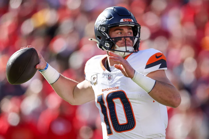 Predictions - Spieler der Woche - Ein Footballspieler in einem weiß-orangefarbenen Broncos-Trikot mit der Nummer 10, Bo Nix, bereitet sich darauf vor, einen Football zu werfen. Er trägt einen schwarzen Helm mit Frontschild. Der Hintergrund ist verschwommen und zeigt eine Menschenmenge in roter Kleidung. Diese Beschreibung wurde mit der FootballR KI automatisch generiert.