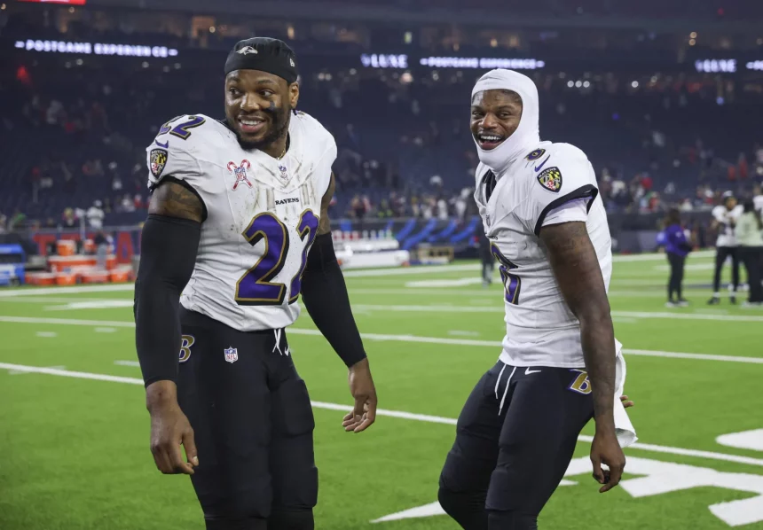 NFL Playoffs: Zwei Footballspieler in weißen Trikots und dunklen Hosen der Baltimore Ravens. Derrick Henry trägt eine schwarze Kappe und das Trikot mit der Nummer 22, während sein Teamkollege Lamar Jackson eine weiße Kapuze und das Trikot mit der Nummer 8 trägt. Im Hintergrund sorgen verschwommene Zuschauer und Sportgeräte für die Atmosphäre. Diese Beschreibung wurde mit der FootballR KI automatisch generiert.