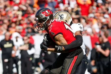 Ein Footballspieler im roten Trikot der Tampa Bay Buccaneers mit der Nummer 13 fängt einen Pass, während er von einem Spieler im weißen Trikot angegriffen wird. Sie sind auf dem Spielfeld, im Hintergrund ist eine verschwommene Menschenmenge zu sehen, die die Action und Intensität dieses spannenden Spiels einfängt. Diese Beschreibung wurde mit der FootballR KI automatisch generiert.