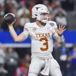 Quinn Ewers in einer weißen Uniform der Texas Longhorns mit der Nummer 3, wahrscheinlich Quinn Ewers, ist bereit, einen Football zu werfen. Er trägt einen weißen Helm mit dem ikonischen Logo der Longhorns und steht in der Mitte des Feldes, umgeben von verschwommenen Zuschauern im Hintergrund. Diese Beschreibung wurde mit der FootballR KI automatisch generiert.