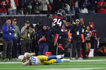 Ein Footballspieler in blau-weißer Uniform wird von einem anderen Spieler mit der Nummer 24, Derek Stingley Jr., zu Boden gerissen. Zuschauer und Fotografen fangen das intensive Spiel auf dem grünen Feld mit sichtbaren Yard-Linien ein. Diese Beschreibung wurde mit der FootballR KI automatisch generiert.