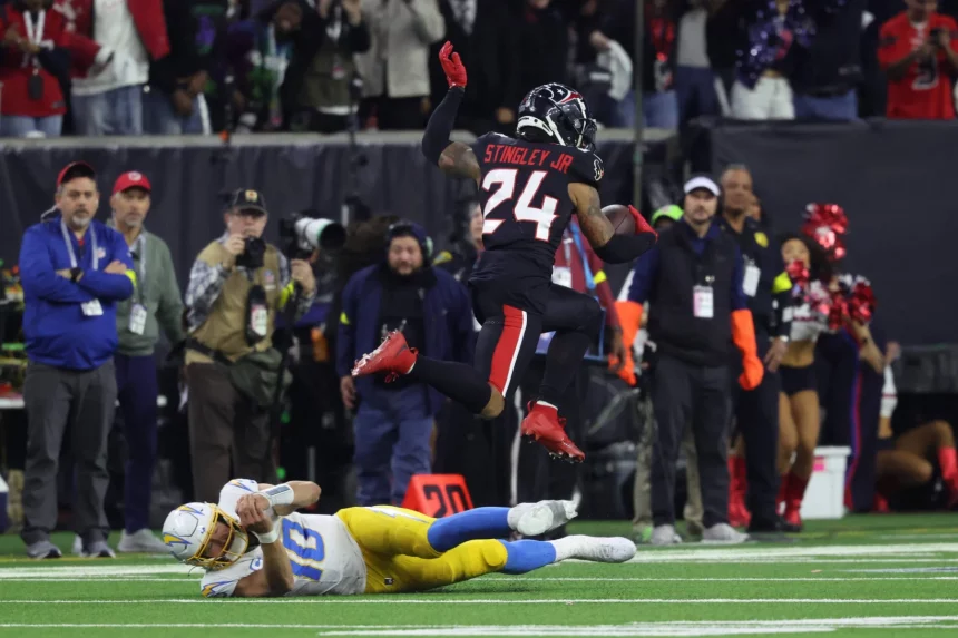 Ein Footballspieler in blau-weißer Uniform wird von einem anderen Spieler mit der Nummer 24, Derek Stingley Jr., zu Boden gerissen. Zuschauer und Fotografen fangen das intensive Spiel auf dem grünen Feld mit sichtbaren Yard-Linien ein. Diese Beschreibung wurde mit der FootballR KI automatisch generiert.