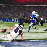 NFL Playoffs Divisional Round - Ein Footballspieler mit der Nummer 89 und der Aufschrift „ANDREWS“ hechtet in einem spannenden NFL-Playoff-Divisional-Round-Spiel in Richtung Endzone und streckt sich nach dem Ball, der gerade außer Reichweite ist. Spieler in blauen Trikots und ein Schiedsrichter sind im Hintergrund zu sehen, während die Zuschauer die Tribünen unter Stadionbeleuchtung füllen. Diese Beschreibung wurde mit der FootballR KI automatisch generiert.
