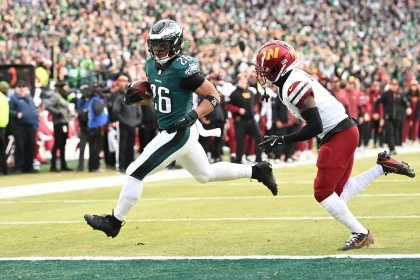 Ein Footballspieler im Trikot der Philadelphia Eagles, Saquon Barkley (Nummer 26), rennt während des Super Bowl LIX in Richtung Endzone. Ein rot-weiß uniformierter Gegner kämpft darum, ihn einzuholen, während die Menge im Stadion zu einer verschwommenen Kulisse für diesen spannenden Moment wird. Diese Beschreibung wurde mit der FootballR KI automatisch generiert.