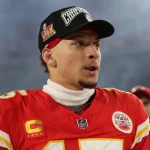 Footballspieler Patrick Mahomes steht in der roten Uniform der Kansas City Chiefs auf dem Feld und trägt eine schwarze Mütze mit dem Schriftzug „Super Bowl Champions“. Er trägt einen weißen Rollkragenpullover und ein rotes Trikot mit der Nummer 15, umgeben von verschwommenen Stadionlichtern und jubelnden Zuschauern im Hintergrund. Diese Beschreibung wurde mit der FootballR KI automatisch generiert.