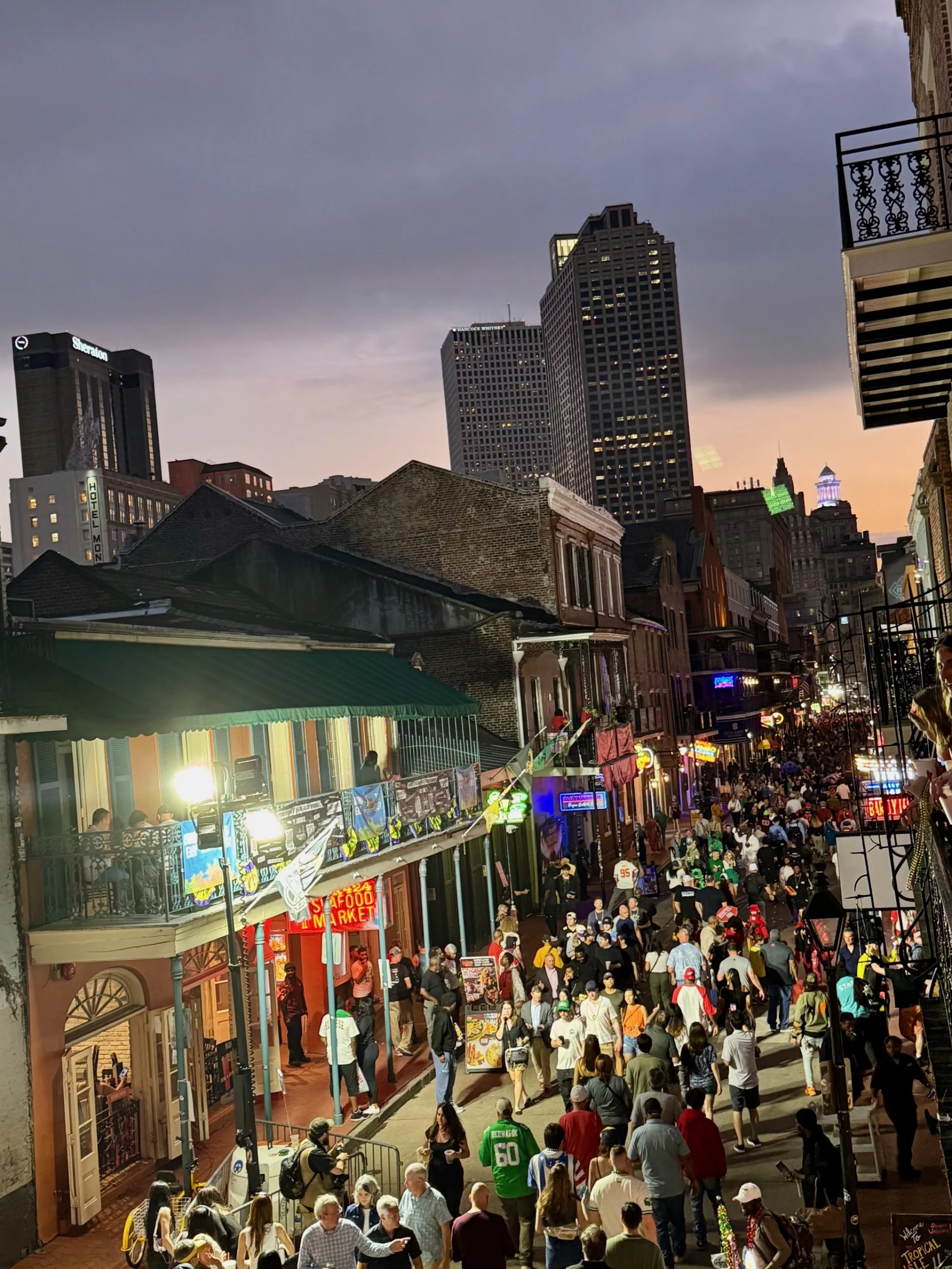 Super Bowl LIX - Eine geschäftige Straßenszene am Abend mit Menschenmassen, die eine belebte Stadtstraße entlanglaufen. Gebäude mit Balkonen sind mit bunten Lichtern und Schildern geschmückt, auf denen stolz Philadelphia Eagles-Banner zu sehen sind. Der Himmel ist bedeckt und im Hintergrund ragen die Wolkenkratzer der Stadt empor. Die Atmosphäre ist lebendig und festlich. Diese Beschreibung wurde mit der FootballR KI automatisch generiert.