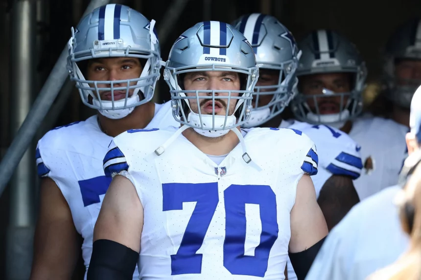 In einem Tunnel stehen die Dallas Cowboys vereint in ihren Uniformen. In der Mitte trägt Zack Martin einen Helm mit Gesichtsschutz und zeigt stolz die Nummer 70 auf seinem Trikot. Hinter ihm bereiten sich seine Mitspieler darauf vor, das Spielfeld zu stürmen. Diese Beschreibung wurde mit der FootballR KI automatisch generiert.